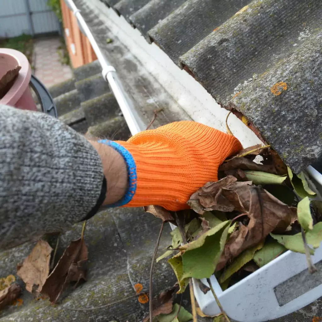 An image of a person cleaning out gutters. Gutters are another part of a roof sytem.