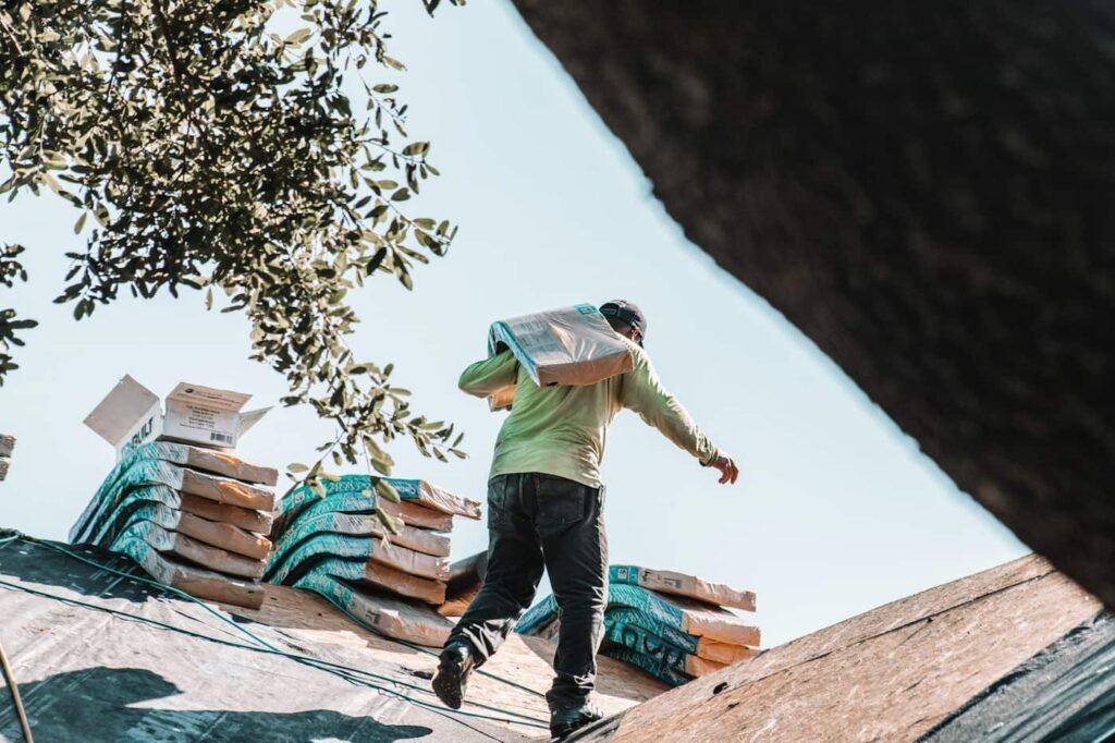 Man carrying bundle of shingles over his shoudler on a roof 